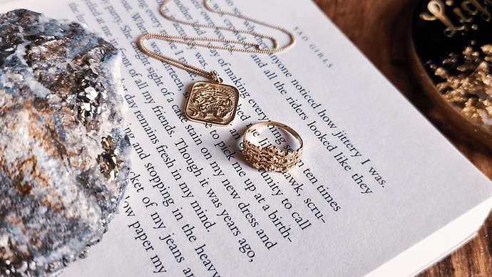 A gold necklace and ring sit utop an opened book's pages.
