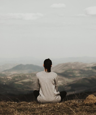 A woman sits with her back towards us whie she looks over a hilly landscape