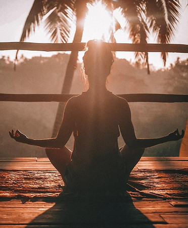 A woman with her back to us sits in the lotus position with the sunset casting her shadow towards us.