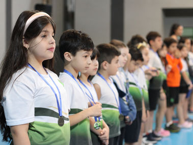Crianças perfiladas com medalhas, em um evento. Escola Erasmo Braga.
