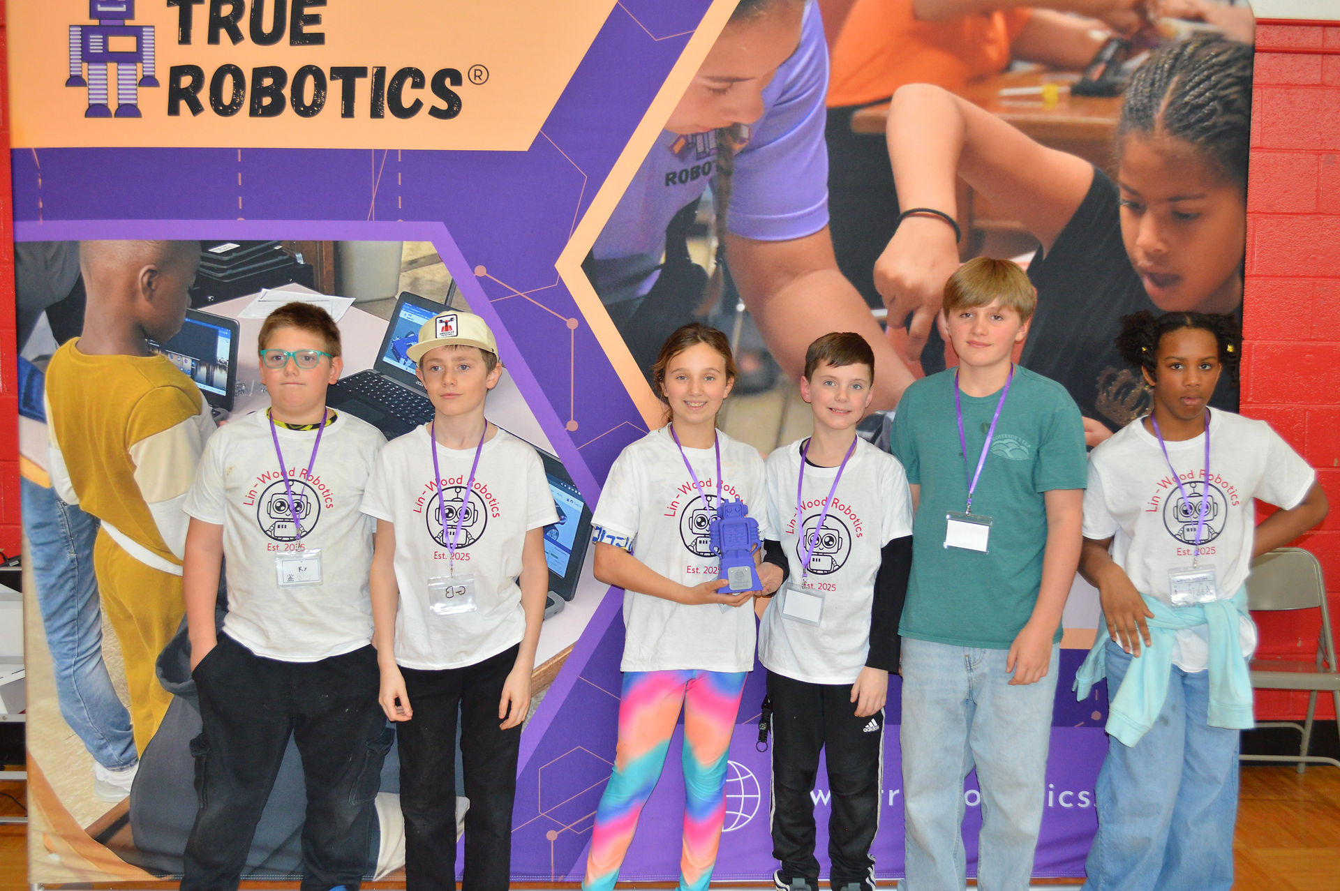 Winning teams proudly hold their trophies, smiling and celebrating their achievements at the robotic