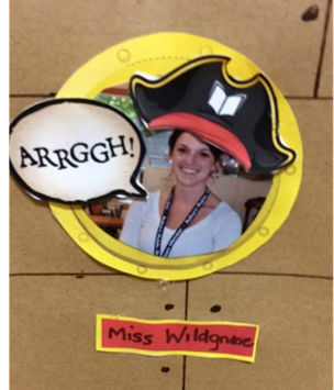 Woman smiling in a pirate-themed photo with a pirate hat and speech bubble saying "ARRGGH!". Background features a circular yellow frame and text "Miss Wildgrube".