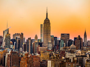New York City skyline at sunset, with the Empire State Building centered against an orange sky and dense high-rise buildings.