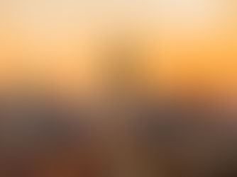 New York City skyline at sunset, with the Empire State Building centered against an orange sky and dense high-rise buildings.