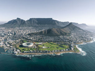 Aerial view of Cape Town with Table Mountain, the waterfront stadium, dense city blocks, and blue ocean under clear skies.