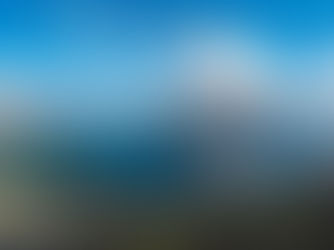Panoramic lake and mountain view over a town and islands under a bright blue sky with clouds.