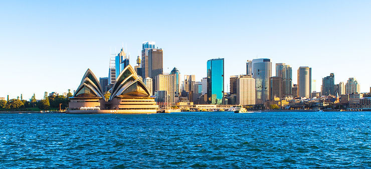 Sydney Opera House and Sydney skyline across blue harbor water on a clear sunny day