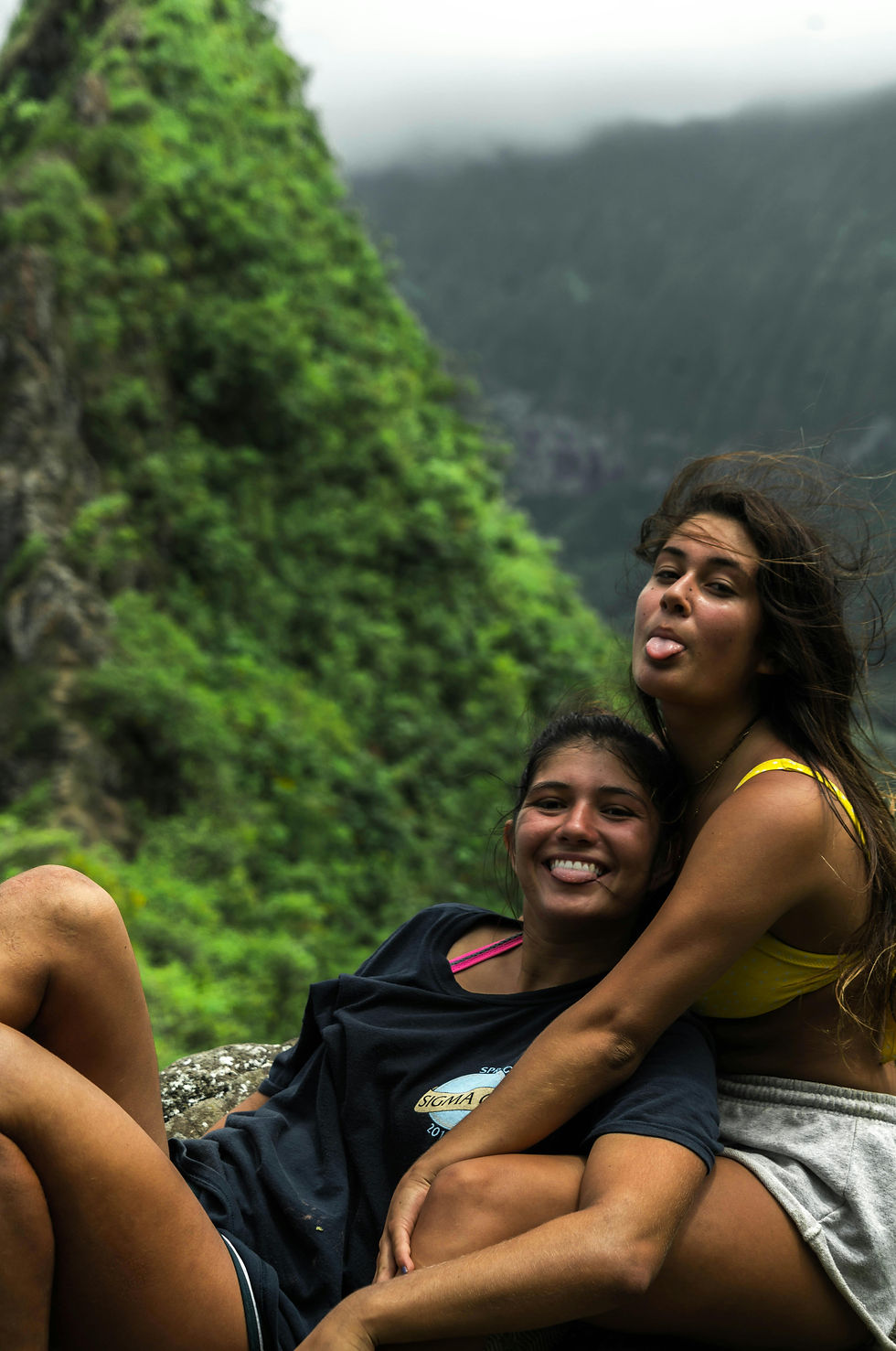 Two friends smile and embrace on top of a beautiful mountainscape.