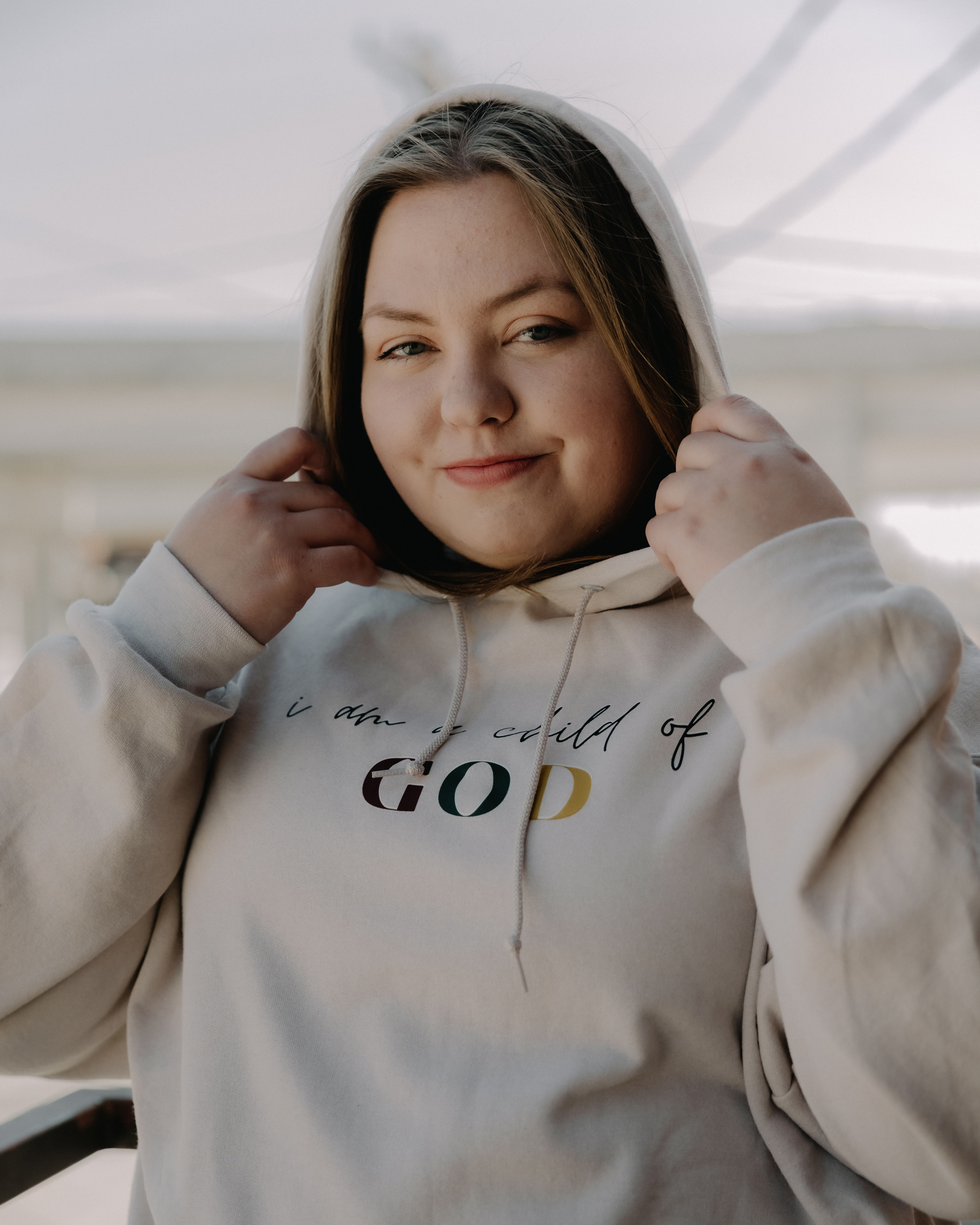 Tan cotton/polyester blend hoodie that says "I am a child of" in cursive letters, and "GOD" in red, blue and yellow letters.
