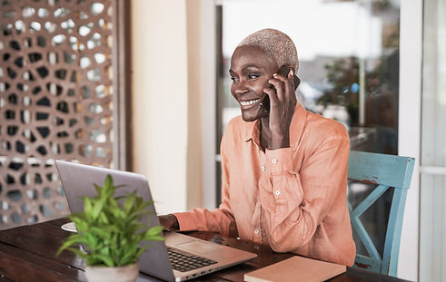 a smiling woman talking on a cellphone while looking at a laptop screen
