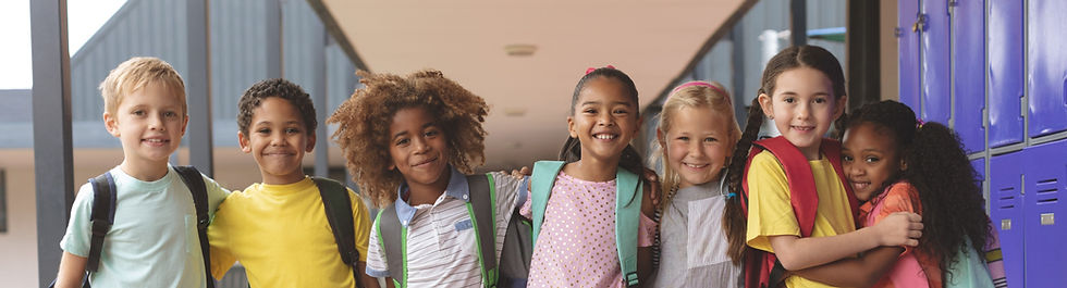 a group of young kids of diferent genders and nationalities smiling at the camera, standing in a school hallway