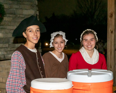 Three children in colonial clothing selling hot chocolate at Yulefest