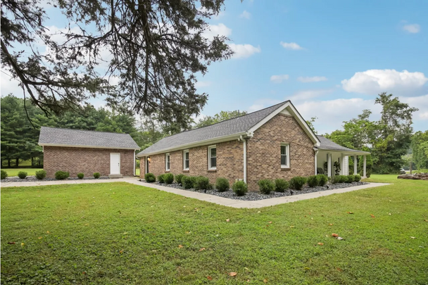 Exterior view of a brick house and detached shed on a green lawn.