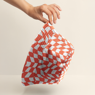 Hand holding a playful orange and white checkerboard bucket hat. Pattern design by Shelby Ruch.