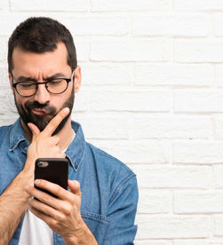 un homme qui regarde son téléphone avec questionnement. Met en lumière le paradoxe entre désir et inaction de l'impact des réseaux sociaux sur le cerveau
