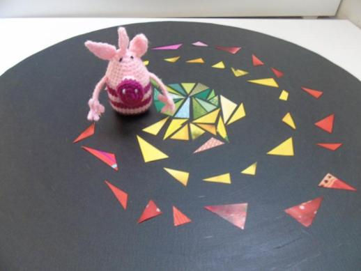 Petit cochon rose en crochet sur un disque noir décoré de triangles colorés en spirale