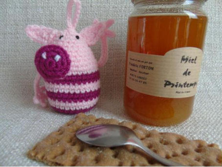 Cochon en crochet rose près d’un pot de miel de printemps, avec une cuillère posée sur des biscuits.