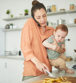 Mère qui tient son bébé tout en préparant à manger et en téléphonant