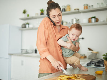 Mère qui tient son bébé tout en préparant à manger et en téléphonant