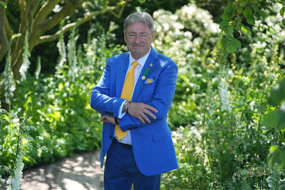 Picture of Alan Titchmarsh wearing a blue suit and yellow tie posing in a garden