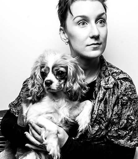 A black and white editorial style portrait of Shel Wyminga and their King Charles Cavalier spaniel, Gomez.