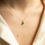 Miniatura: Woman wearing gold necklace with MAY pendant - Emerald - LUMIÈRE on her neck.