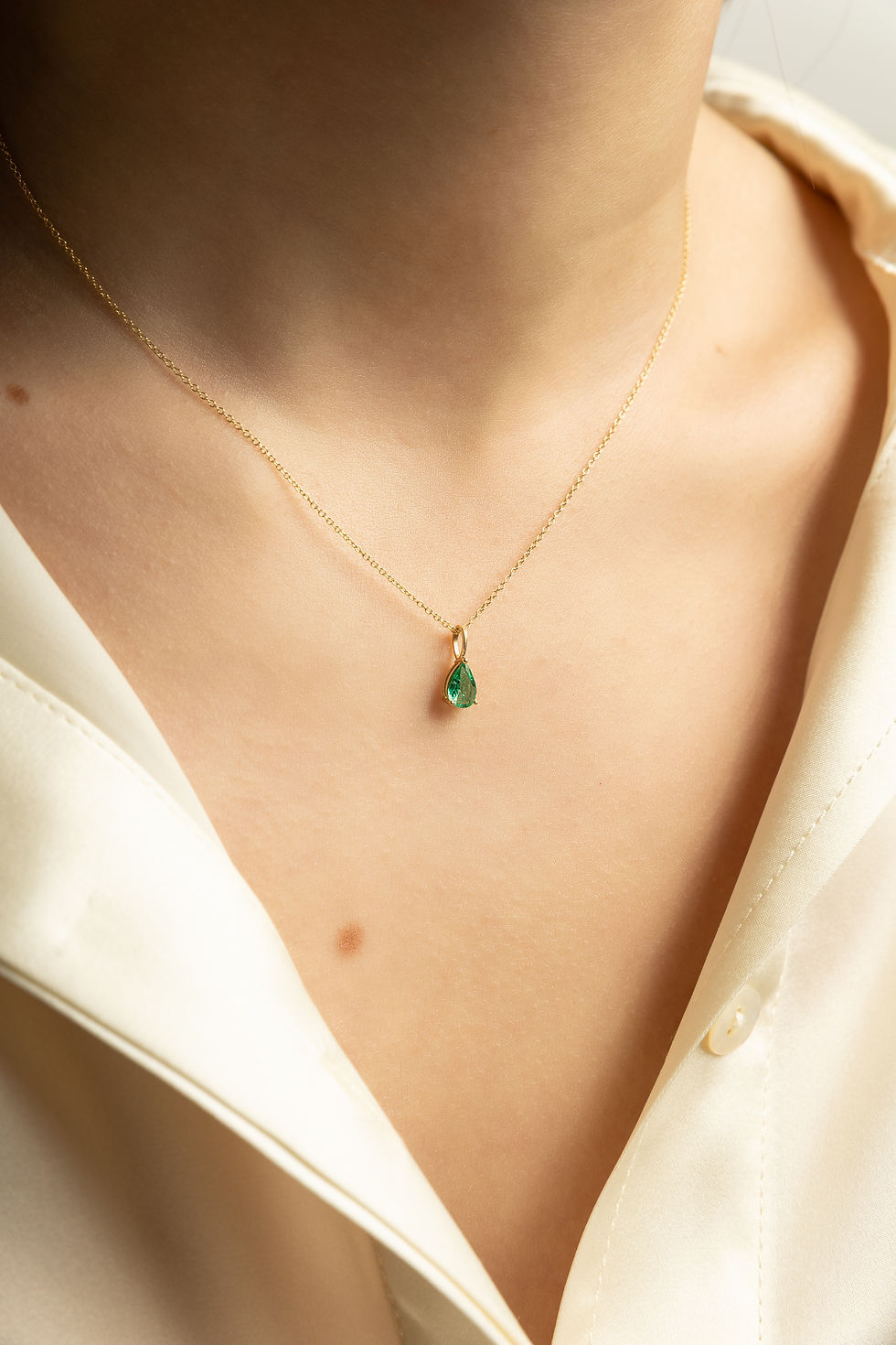Woman wearing gold necklace with MAY pendant - Emerald - LUMIÈRE on her neck.