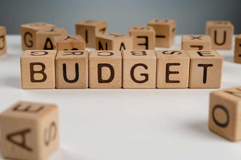 Wooden blocks spelling "BUDGET" on a white surface, with scattered letter blocks in the background, clear and minimalist setting.
