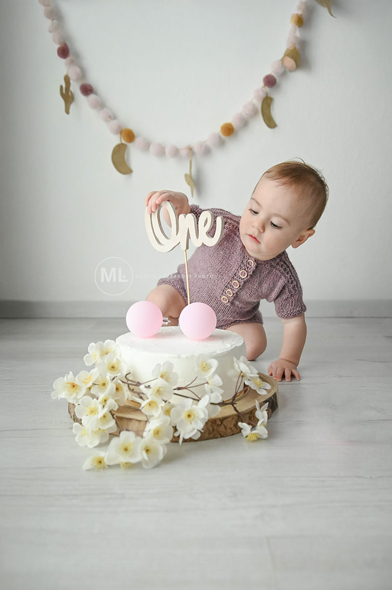 Bambina curiosa con torta di primo compleanno, scritta 'one'