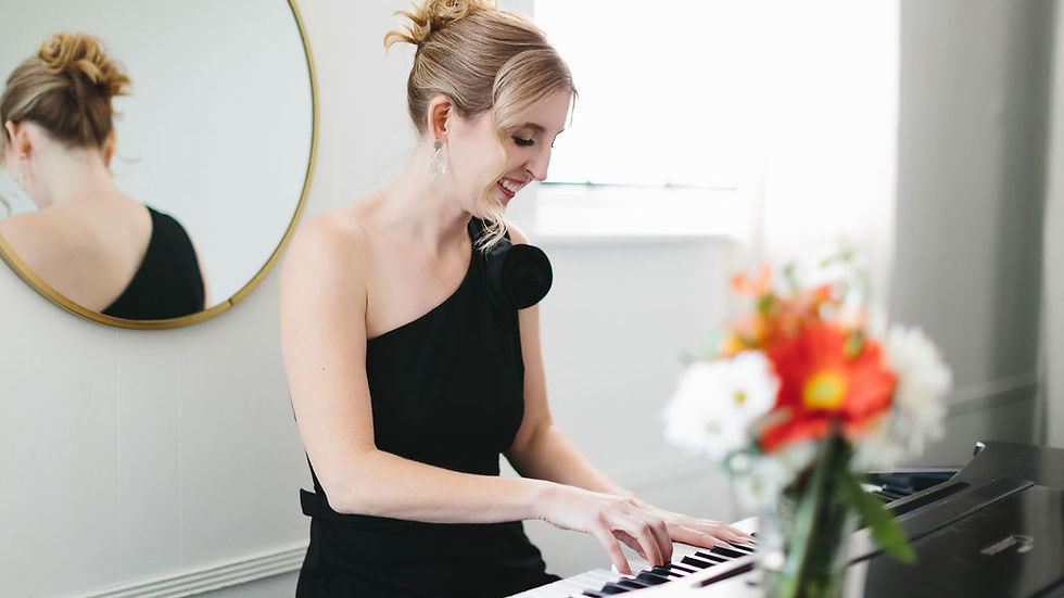 Woman playing the piano while wearing a one shoulder black jumpsuit.