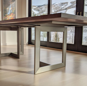 Walnut dining table in a dining room with large windows showing a mountain view. The table has a modern style custom  square base made of brushed steel. The table top is made of a beautiful walnut slab.