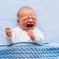 Newborn crying baby boy. New born child tired and hungry in bed under blue knitted blanket