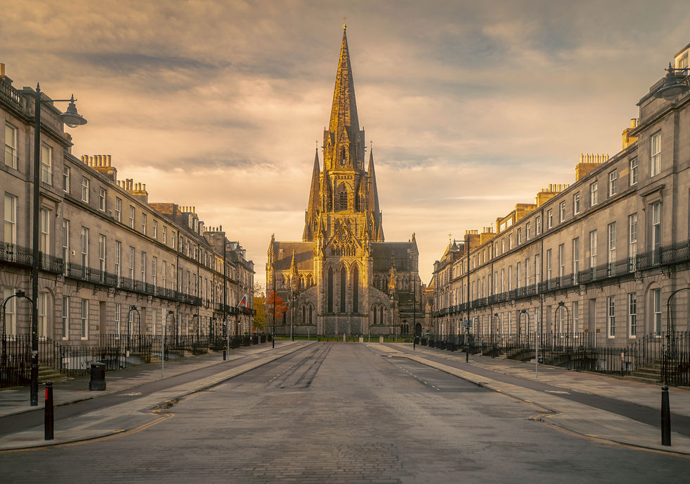 Golden-hour view down a quiet Edinburgh street toward a Gothic church spire, framed by symmetrical stone buildings and a dramatic warm sky.