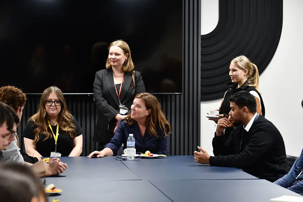Dame Rachel de Souza talking with a small group of around four to six sixth form students of mixed gender and ethnicity in a bright indoor college space at John Leggott College, Scunthorpe.
