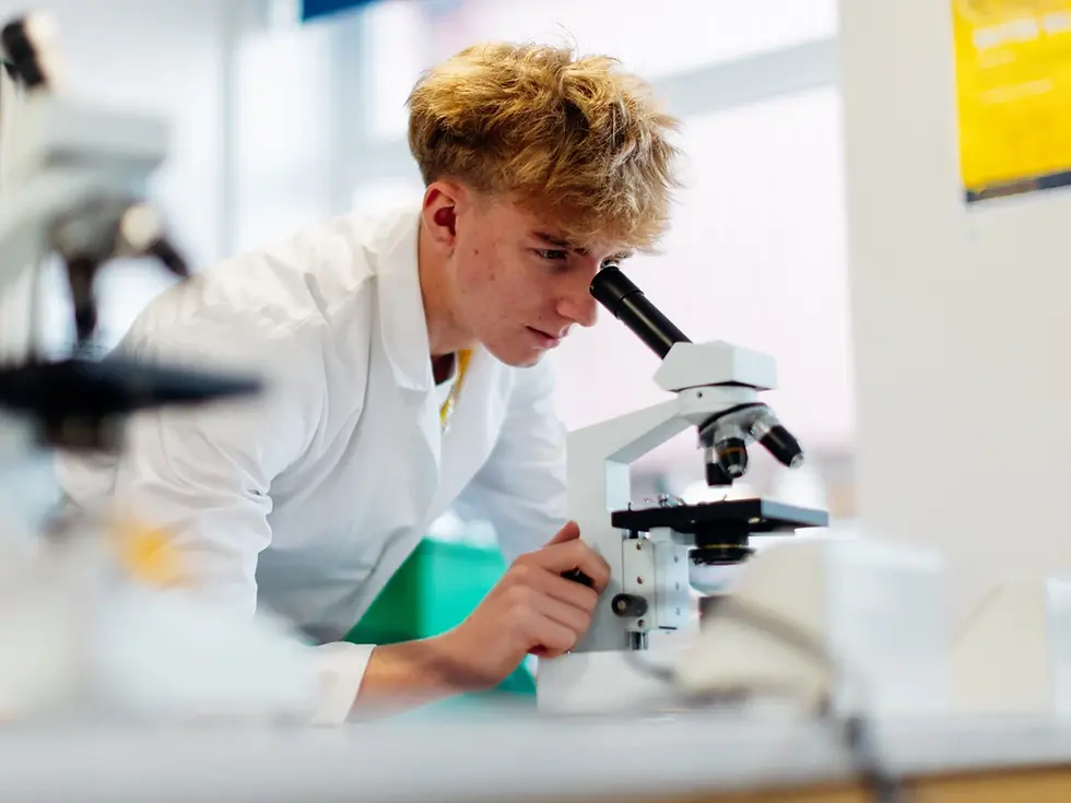 JLC student in a lab white coat studying Biology using a microscope to examine and conduct experiment. 