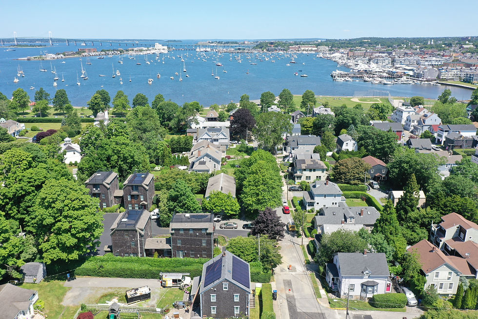 Aerial view of coastal neighborhood with homes and rooftop solar panels overlooking a harbor filled with sailboats