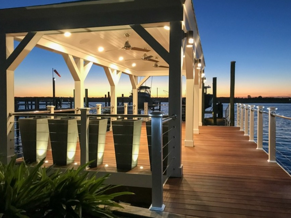 Illuminated white pavilion on a wooden dock at sunset