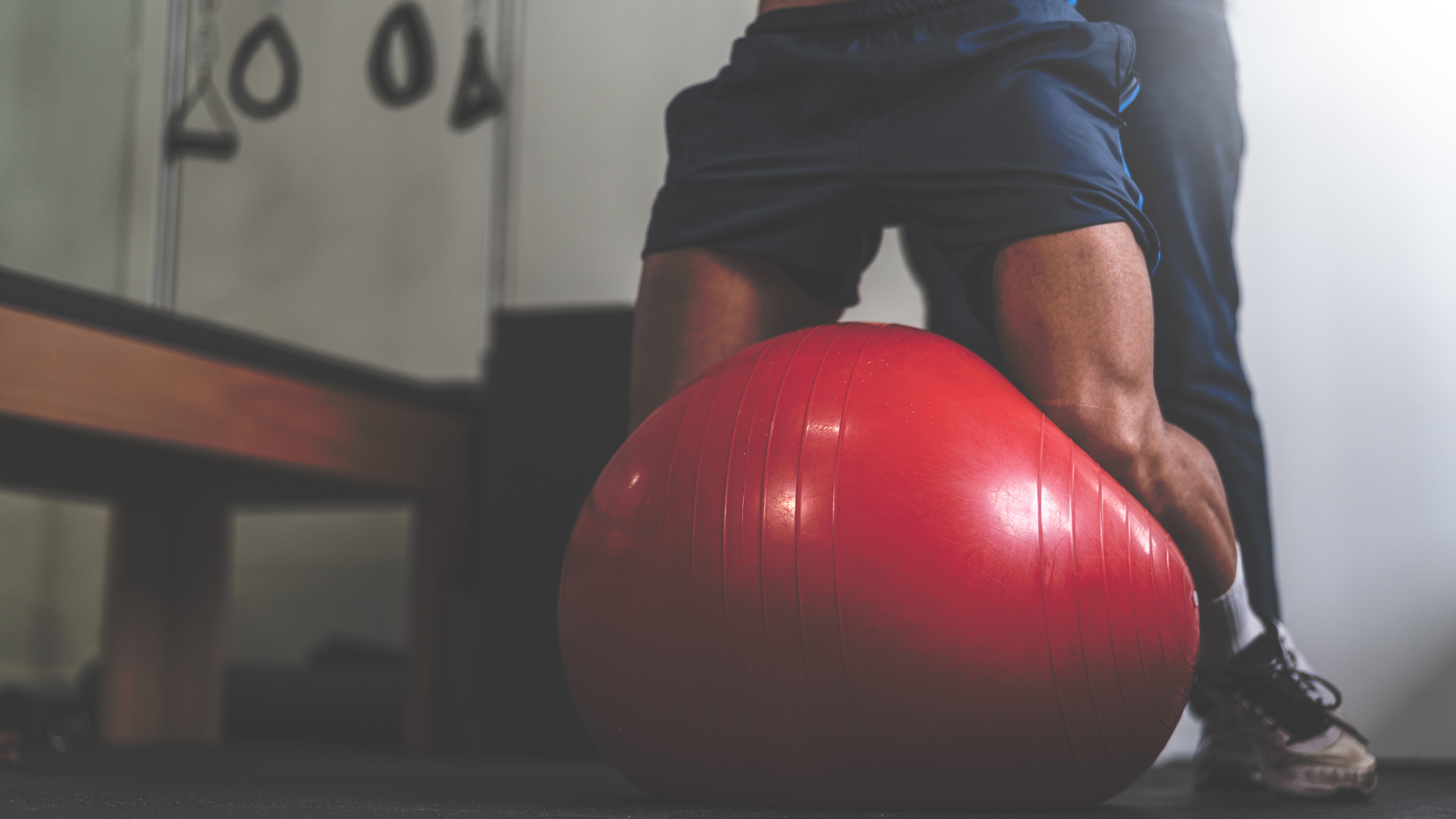 Man lifting red exercise ball, indoor gym setting, workout training