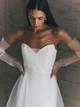 Soft and romantic with a modern edge, Elisa from NEWHITE’s Deja Vu collection is effortlessly ethereal. Featuring a structured yet lightweight bodice with a unique notched neckline, Elisa is crafted in a sheer, textured fabric that gives it a dreamy, airy feel. The detachable sheer sleeves add a soft, fashion-forward detail, perfect for brides who want a versatile and elevated look. Feminine and fresh, Elisa is ideal for the bride who wants something delicate but striking.