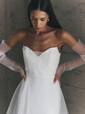 Soft and romantic with a modern edge, Elisa from NEWHITE’s Deja Vu collection is effortlessly ethereal. Featuring a structured yet lightweight bodice with a unique notched neckline, Elisa is crafted in a sheer, textured fabric that gives it a dreamy, airy feel. The detachable sheer sleeves add a soft, fashion-forward detail, perfect for brides who want a versatile and elevated look. Feminine and fresh, Elisa is ideal for the bride who wants something delicate but striking.