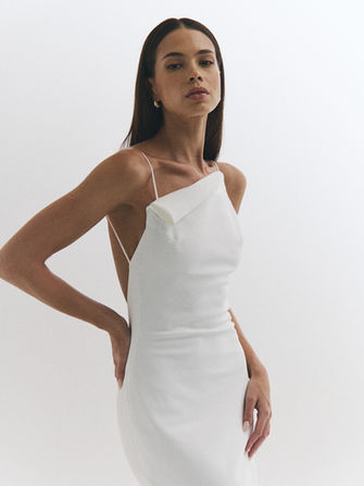 Sleek, modern, and effortlessly cool, Lya from NEWHITE’s Deja Vu collection is a minimalist dream. This one-shoulder gown features a clean, body-skimming silhouette with an asymmetrical neckline and delicate strap detail that gives it an understated edge. Crafted from smooth, structured fabric, Lya is perfect for the bride seeking a sophisticated, fashion-forward look that feels timeless yet unexpected.