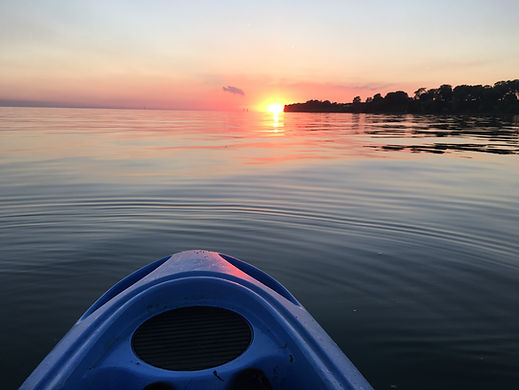 View from a blue kayak on calm Lake Erie during a stunning sunset, paddling near The Lakeside House shoreline