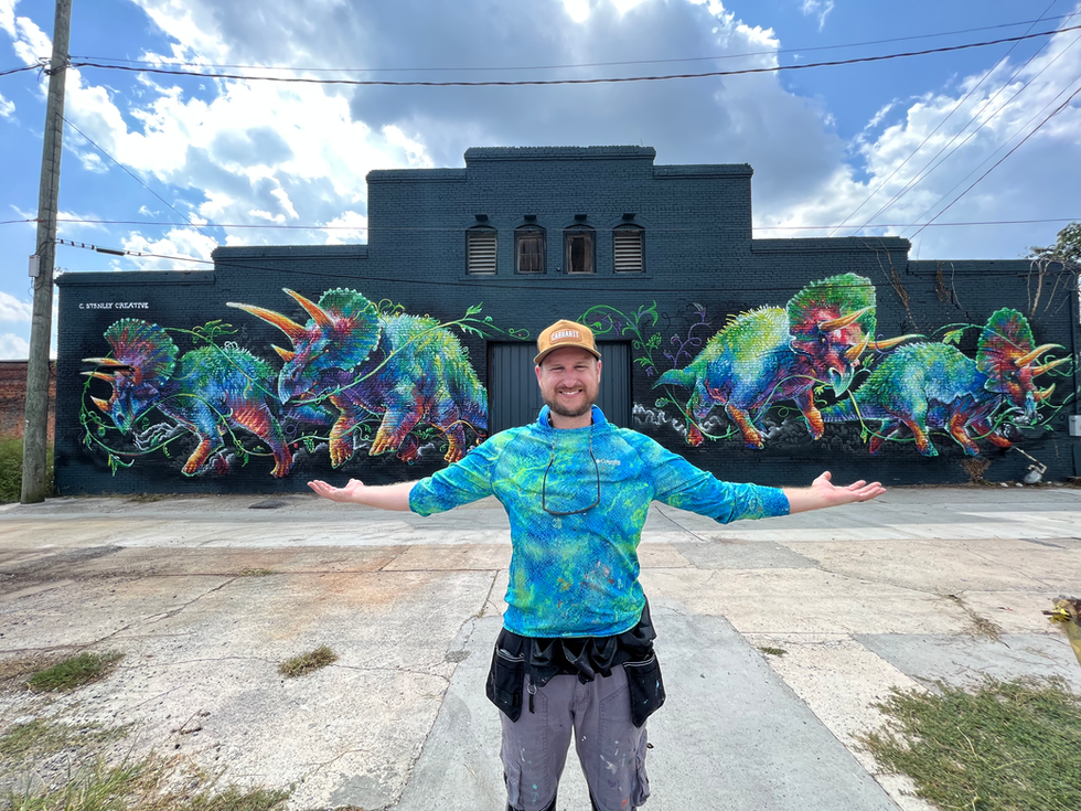 This mural features four colorful triceratops dinosaurs wrapped in hop vines. It is located in Macon, GA and was painted in 2023 by artist Christian Stanley.