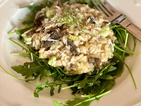 Krämig svamprisotto på ruccolabädd på vit tallrik, toppad med parmesan och timjan, med gaffel vid sidan.