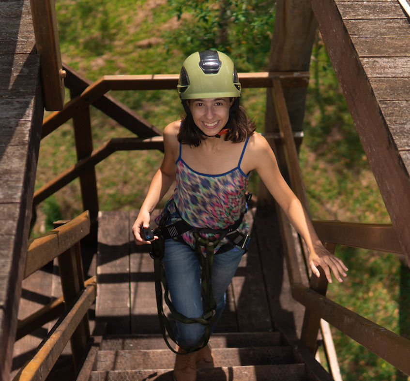 Mulher sorrindo e usando equipamentos de segurança para tirolesa em meio a floresta no Hotel Fazenda Morros Verdes Ecolodge em Ibiúna SP