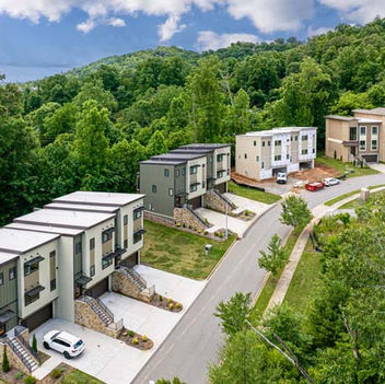 Aerial view of modern townhomes along a curved street surrounded by lush green hills – Buchanan Construction, Asheville.