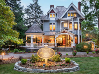 Grand historic inn with a wraparound porch and warm evening lights surrounded by gardens — Asheville Bed and Breakfast Association, Asheville, NC.