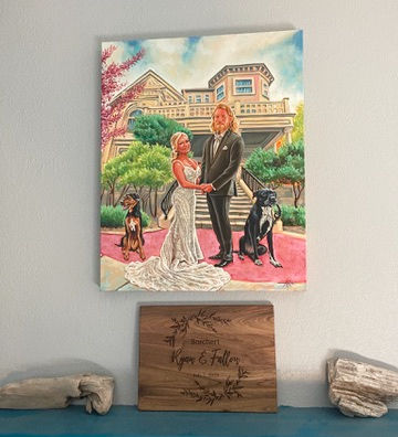 Finished wedding painting hanging in a couple’s home, showing the bride and groom with their dogs in front of a historic building.