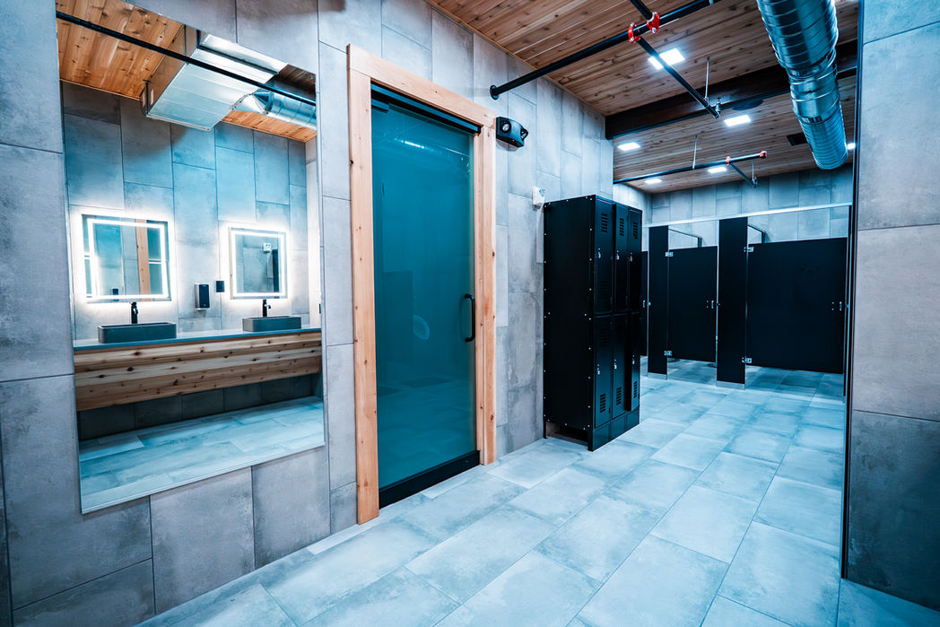 Industrial-style locker room with lighted mirrors and sinks.