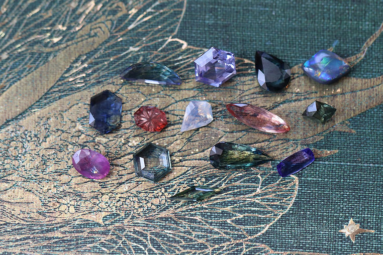 Various natural faceted colored gemstones on a green and gold background.
